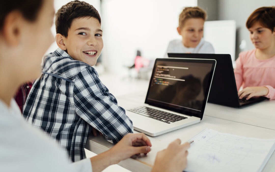 Student coding on laptop looking over shoulder at camera and smiling